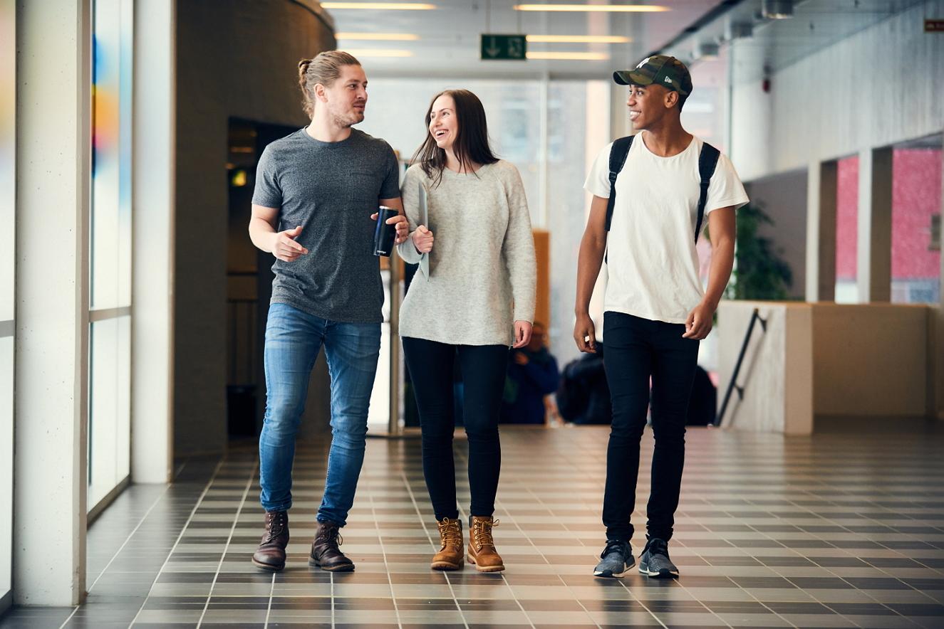 Tre smilende studenter innendørs